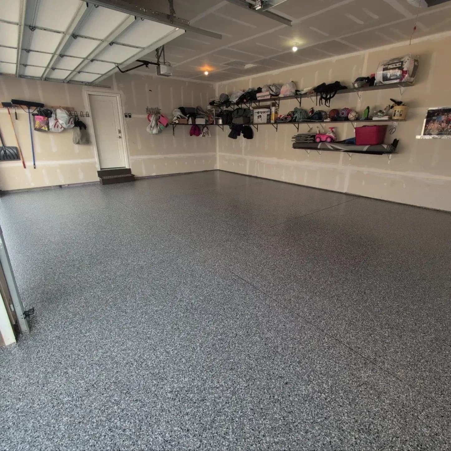 Organized garage interior with gray epoxy flooring, white walls, and shelving units holding sports equipment, bins, and clothing along the walls